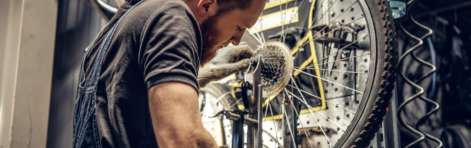 Mechanic removing bicycle rear cassette in a workshop. Red hair bearded mechanic removing bicycle rear cassette in a workshop.